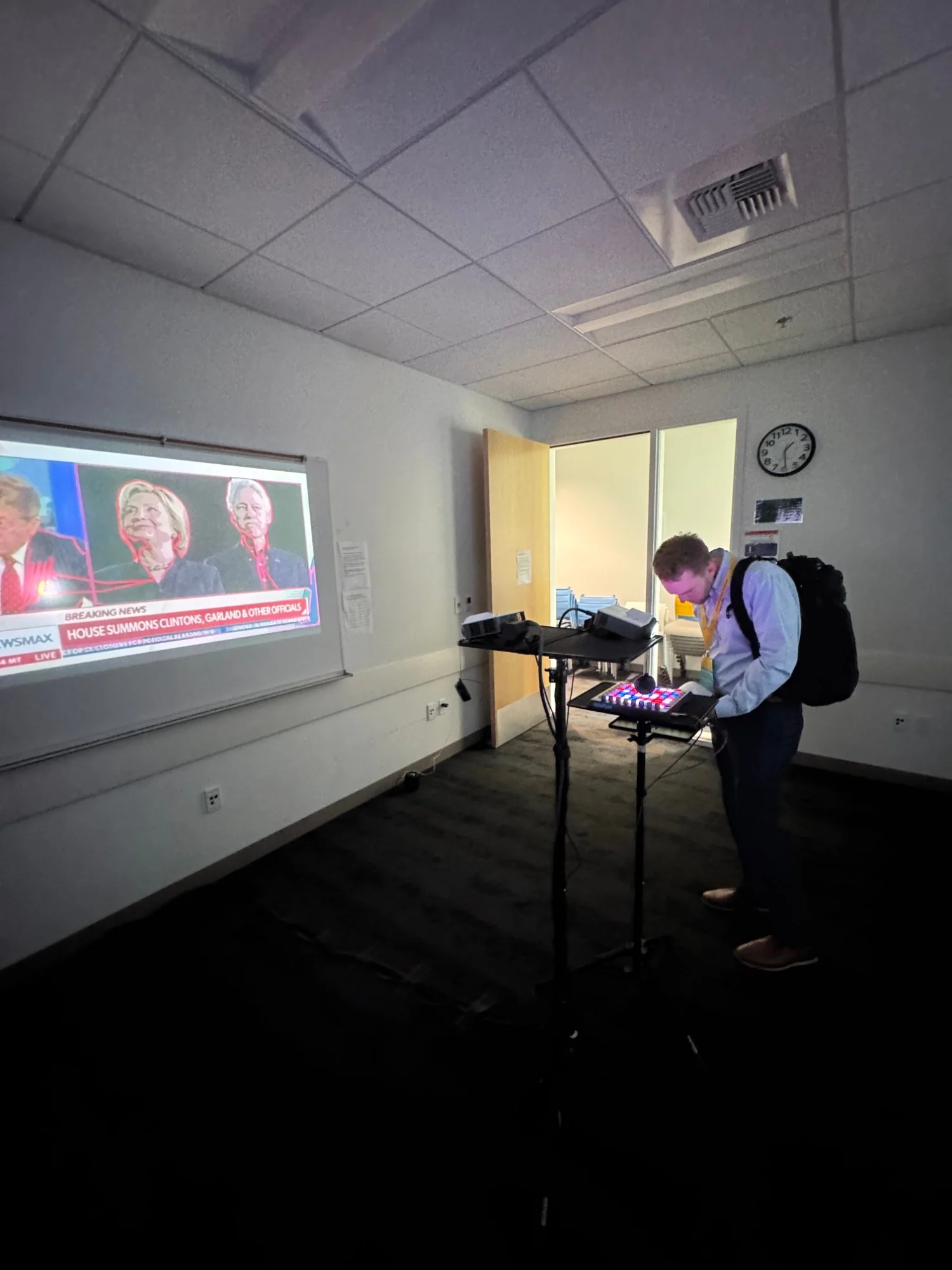 A visitor at the lit pad grid, choosing the next video, beside the projection